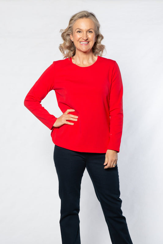 Woman wearing a red sweater and black pants against a white background