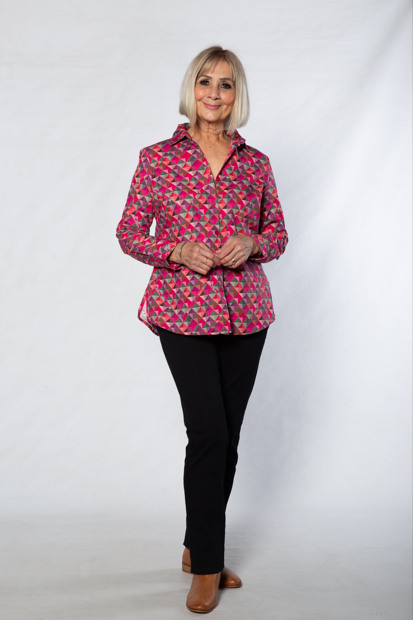 Woman wearing a pink patterned blouse and black pants on a white background