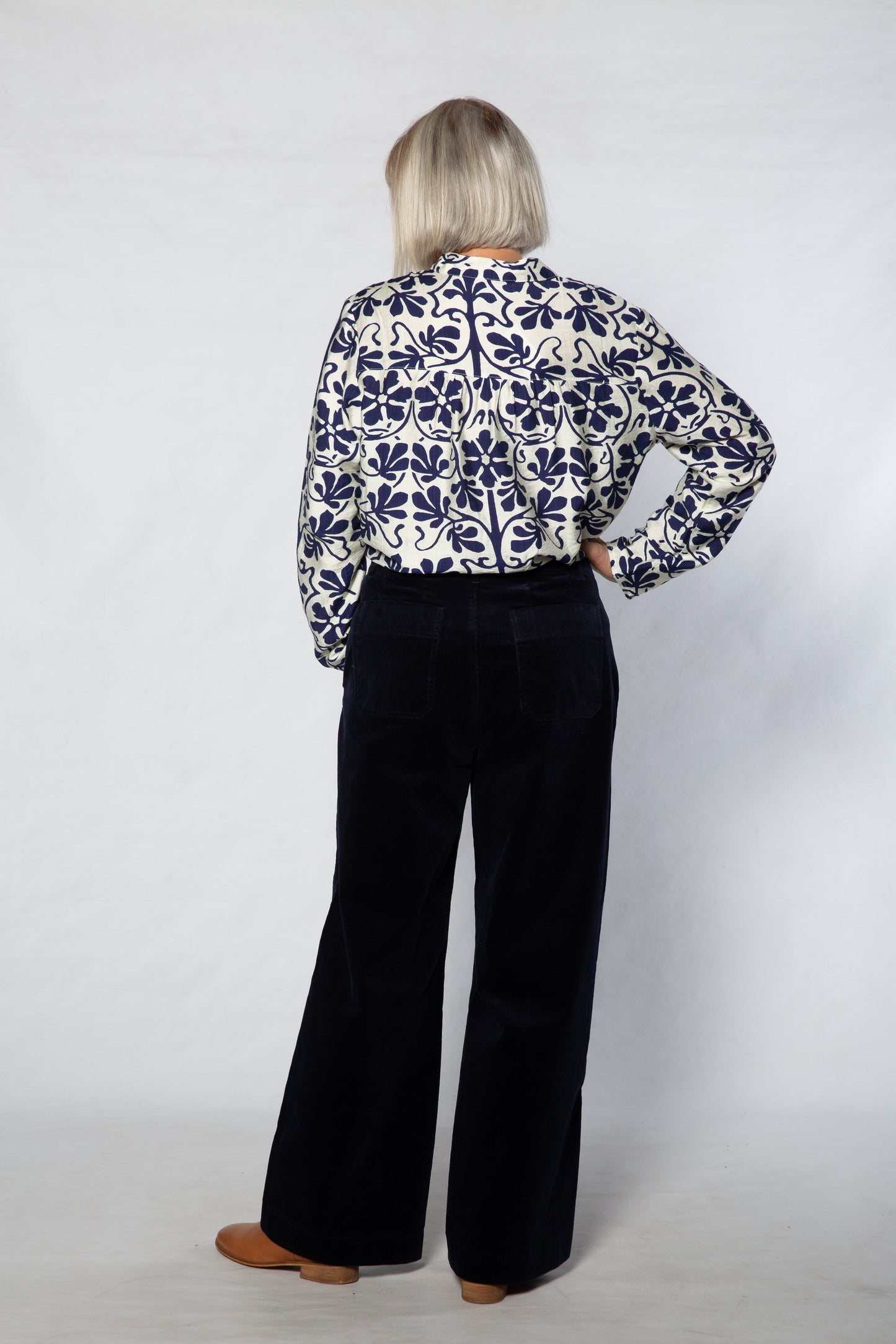 Person wearing a patterned blouse and black pants on a white background