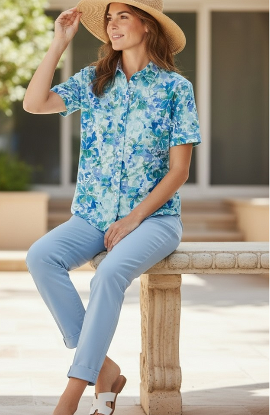 Woman wearing a blue floral shirt and light blue pants, sitting on a wooden bench outdoors.