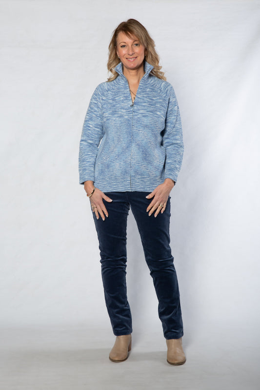 Woman wearing a blue patterned sweater and dark jeans against a white background