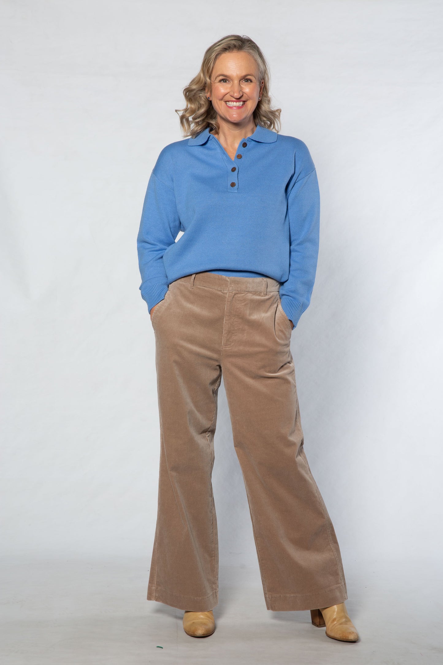 Woman wearing a blue shirt and brown pants against a white background