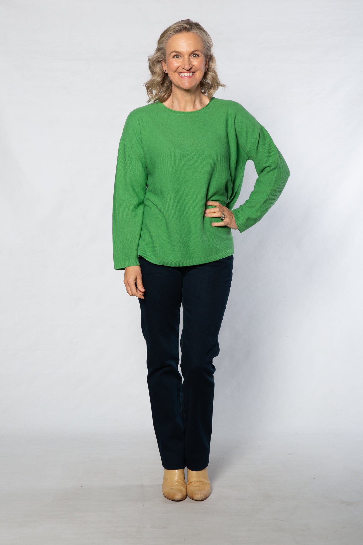 Person wearing a green sweater and black pants on a white background