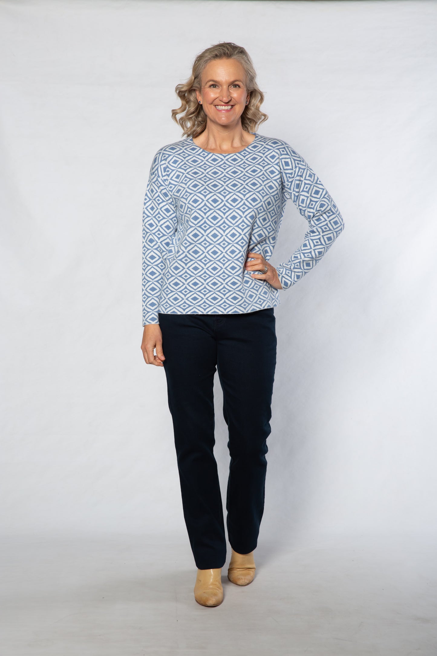 Woman wearing a blue patterned sweater and dark pants on a white background