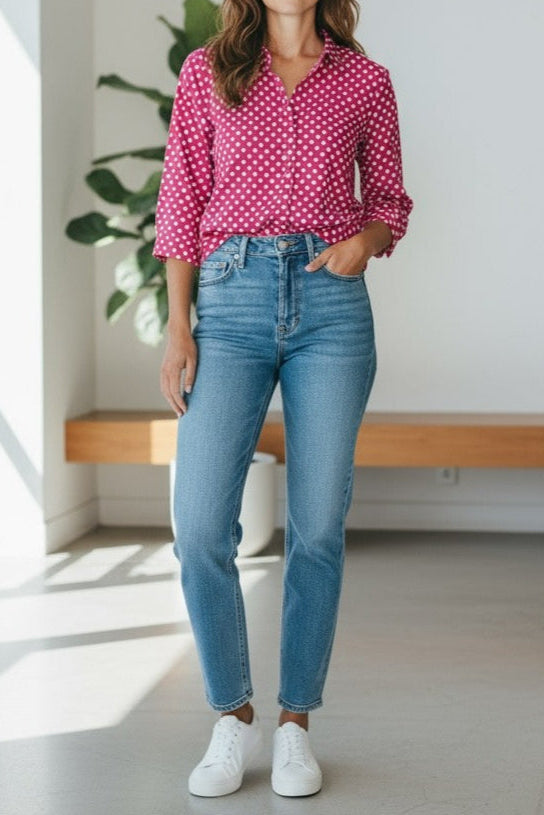 Person wearing a pink polka dot shirt, blue jeans, and white sneakers in a bright room.