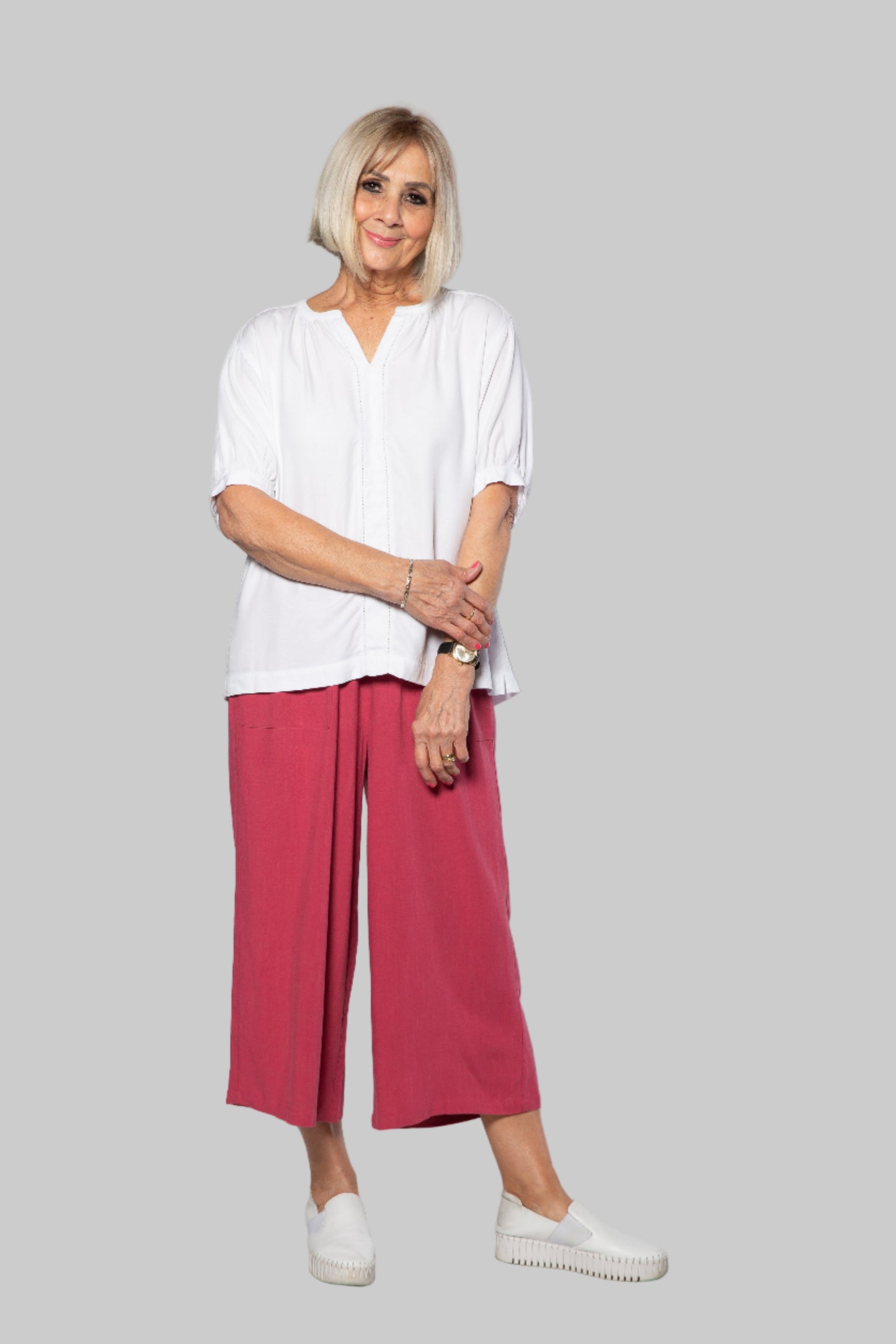 Woman wearing a white blouse and pink pants against a white background
