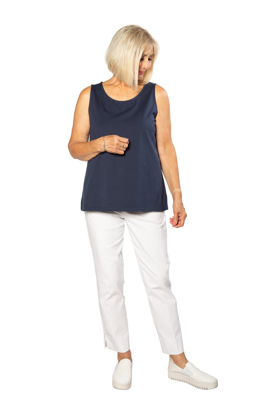 Woman wearing a navy sleeveless top and white pants on a plain background