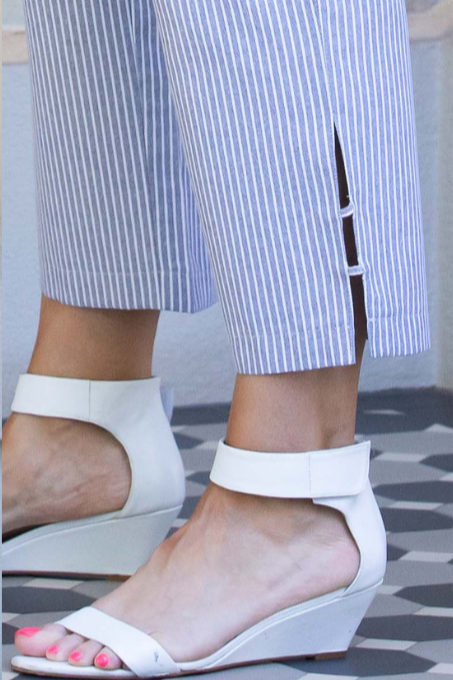 A woman standing outdoors wearing black drawstring stripe pants with side seam hem tab details, paired with a black top and white sandals.