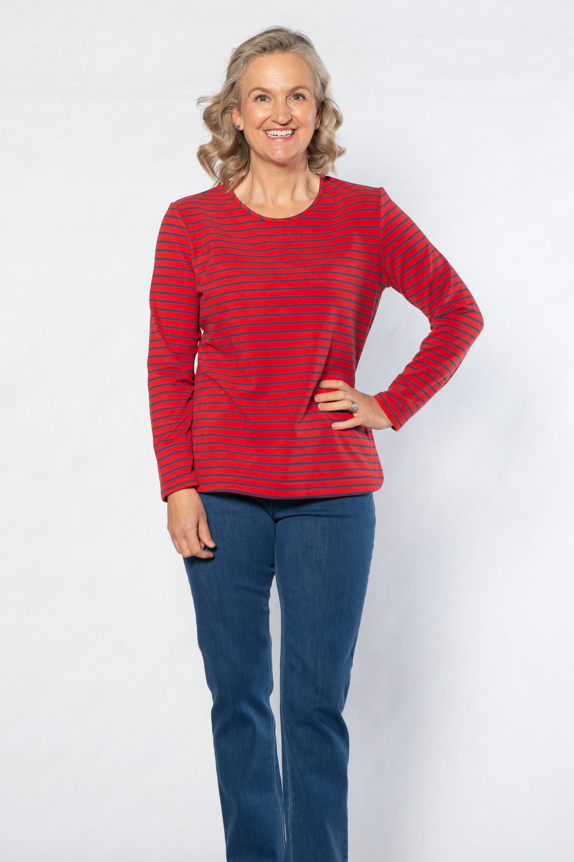 Woman wearing a red striped top and blue jeans standing against a white background