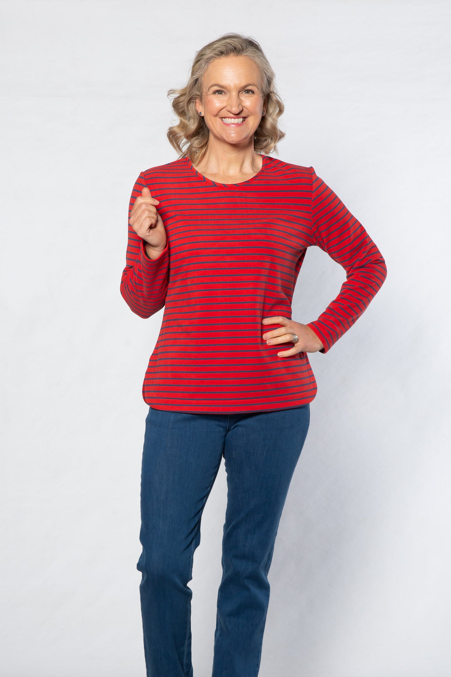 Woman wearing a red striped sweater and blue jeans standing against a white background
