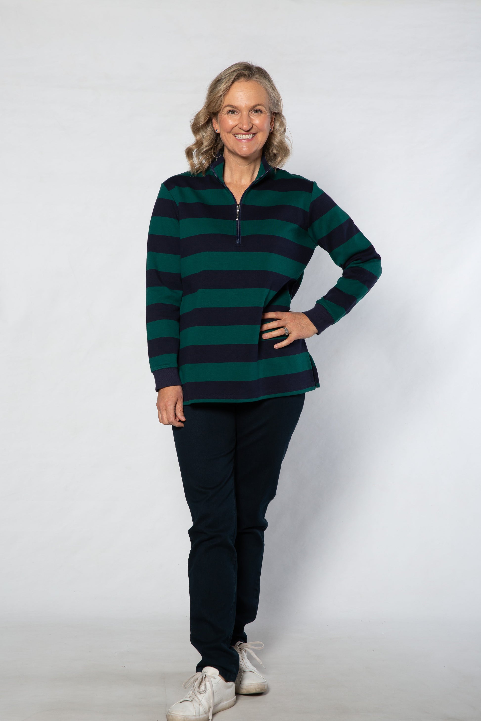Woman wearing a green and navy striped sweater with black pants on a white background