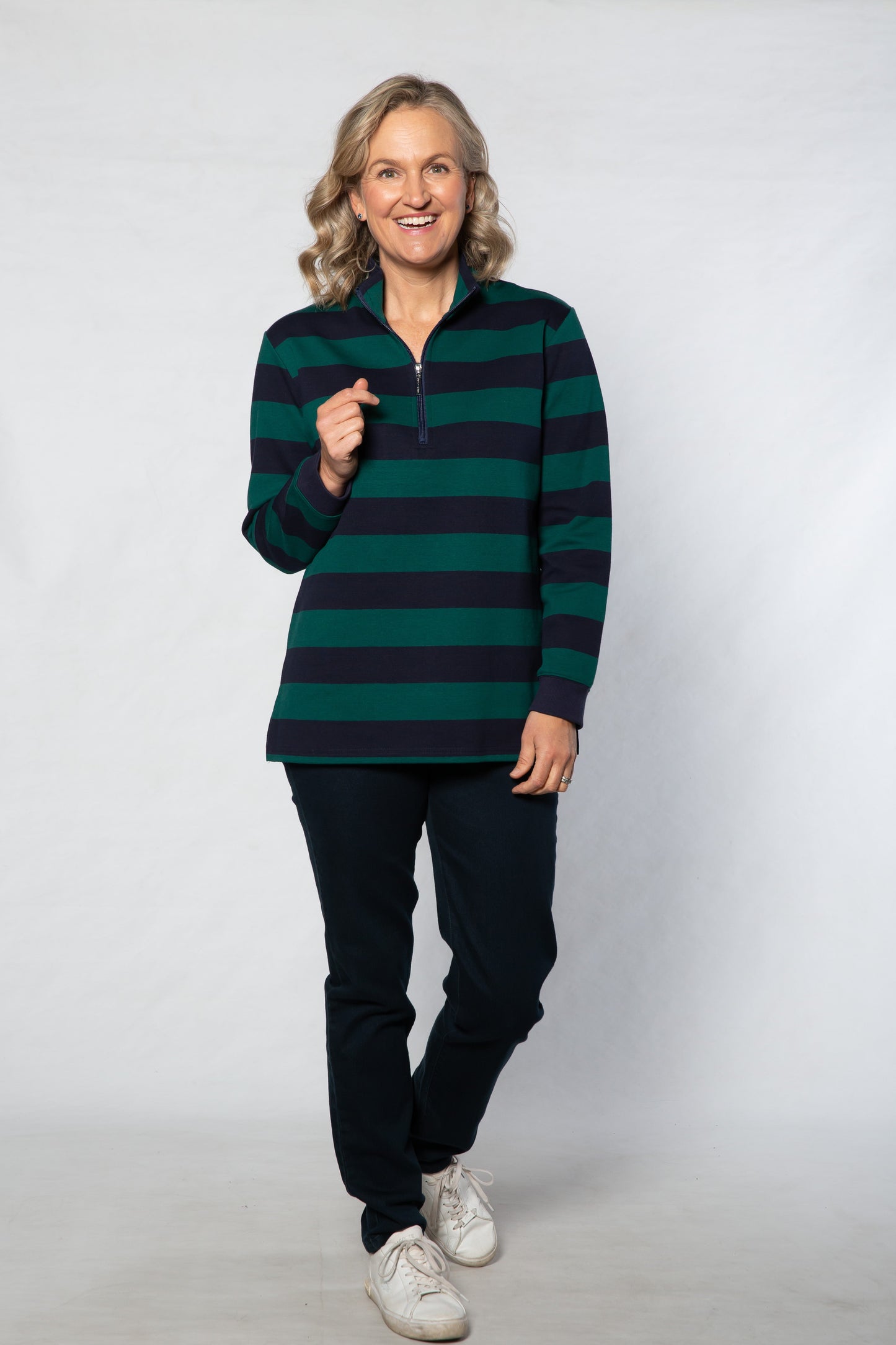 Person wearing a green and navy striped sweater with black pants on a white background