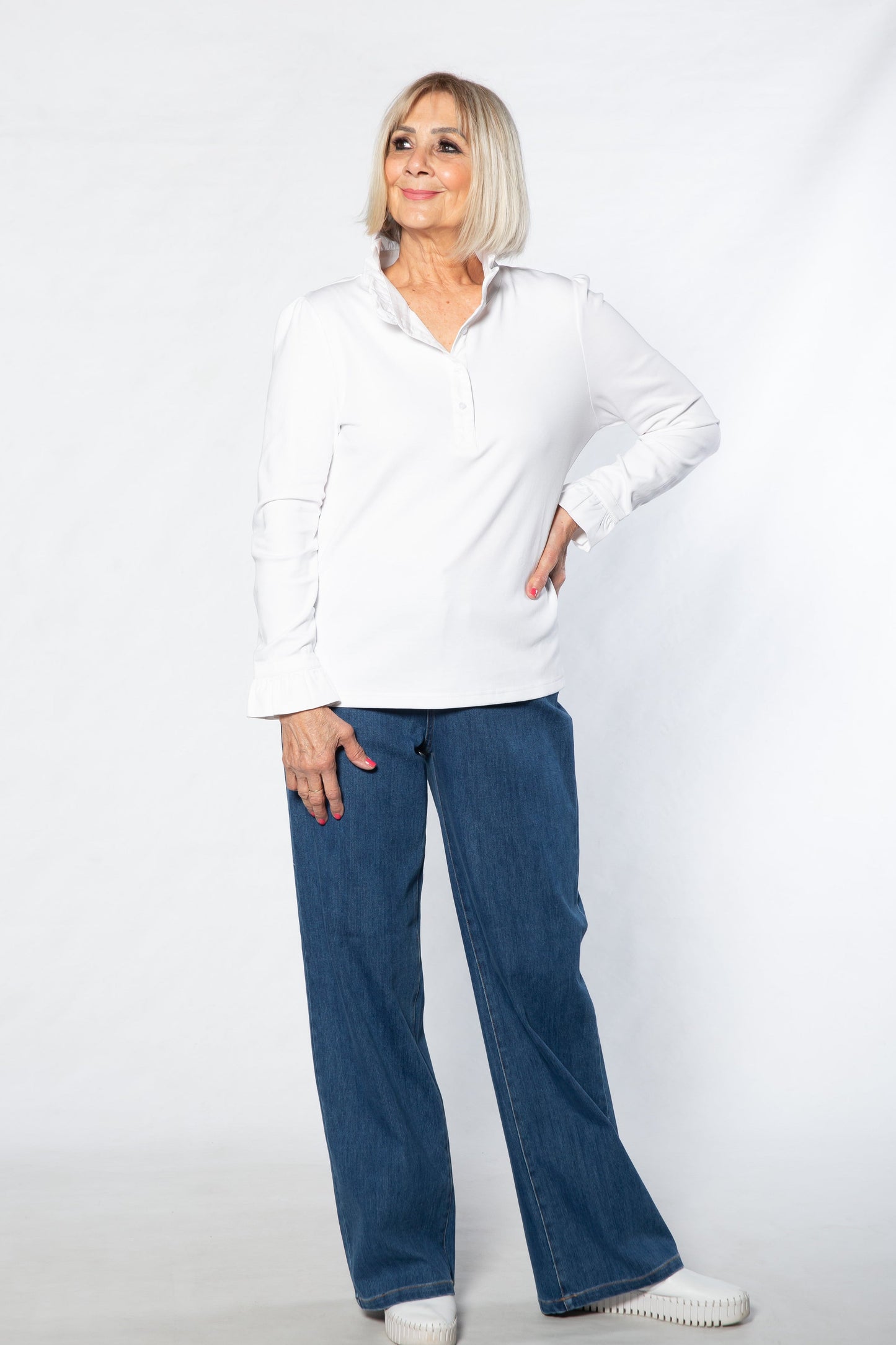 Woman wearing a white shirt and blue jeans standing against a white background