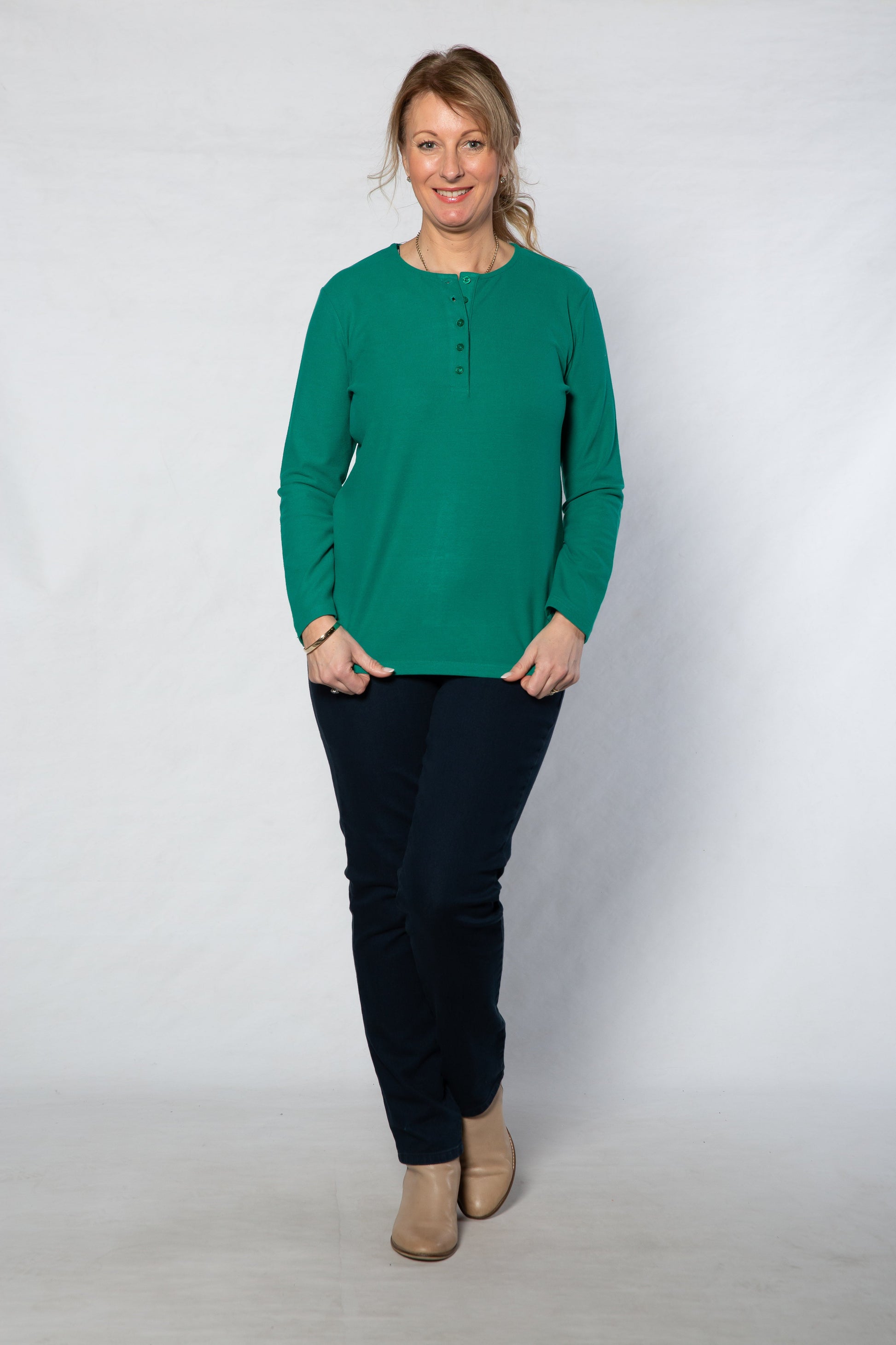 Woman wearing a green long-sleeve shirt and black pants against a white background