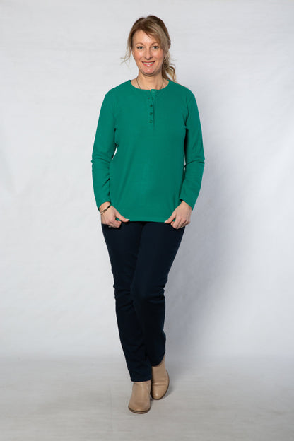Woman wearing a green long-sleeve shirt and black pants against a white background