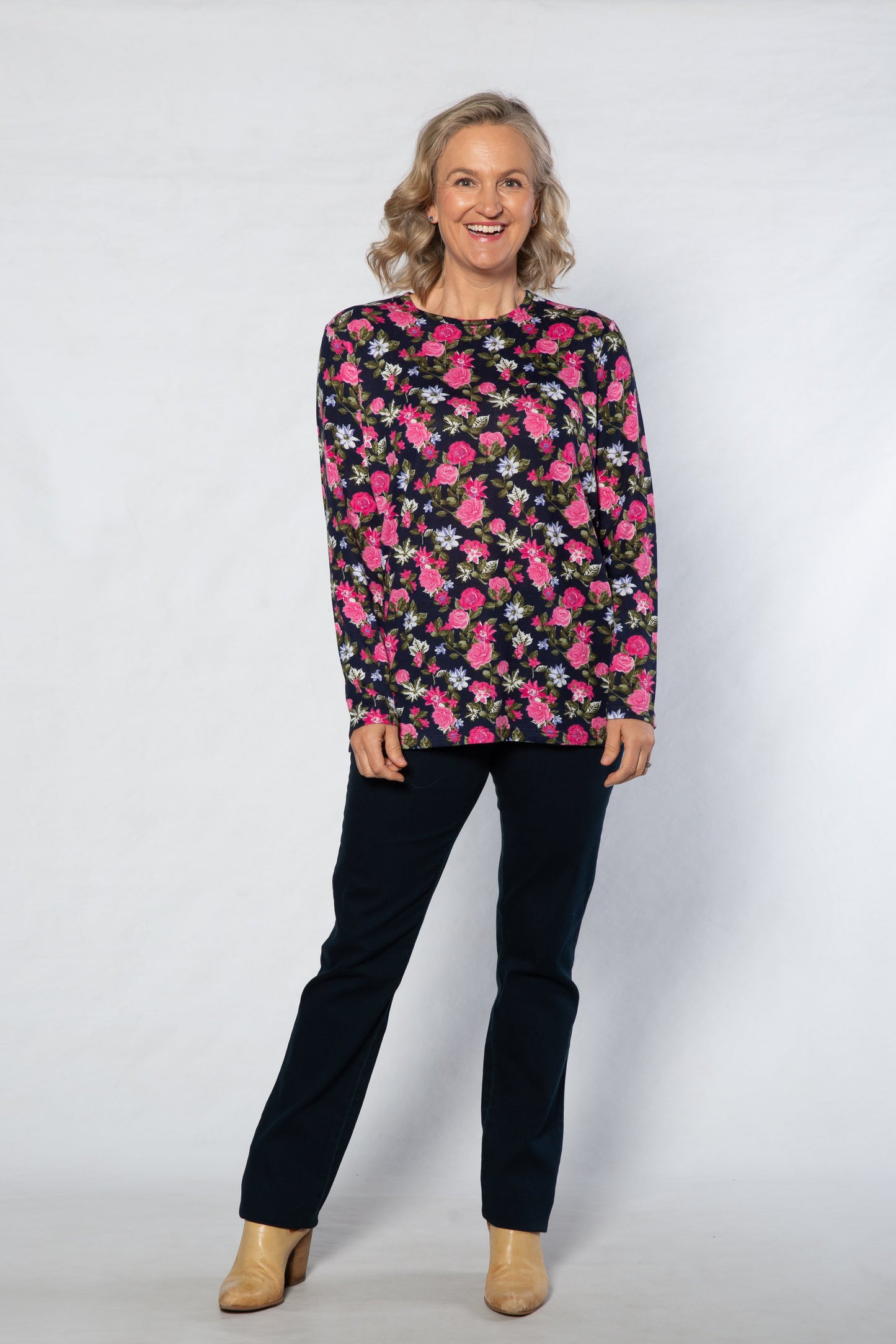 Woman wearing a floral patterned top and black pants on a white background