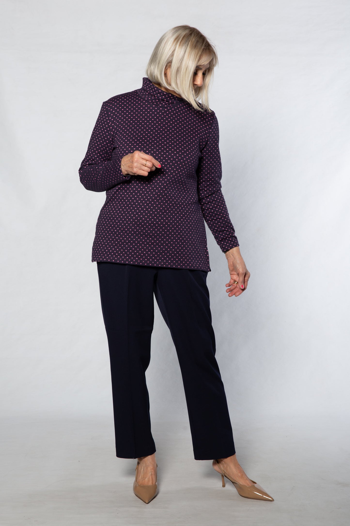 Person wearing a purple polka dot blouse and black pants against a white background