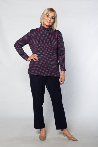 Woman wearing a purple polka dot top and black pants against a white background