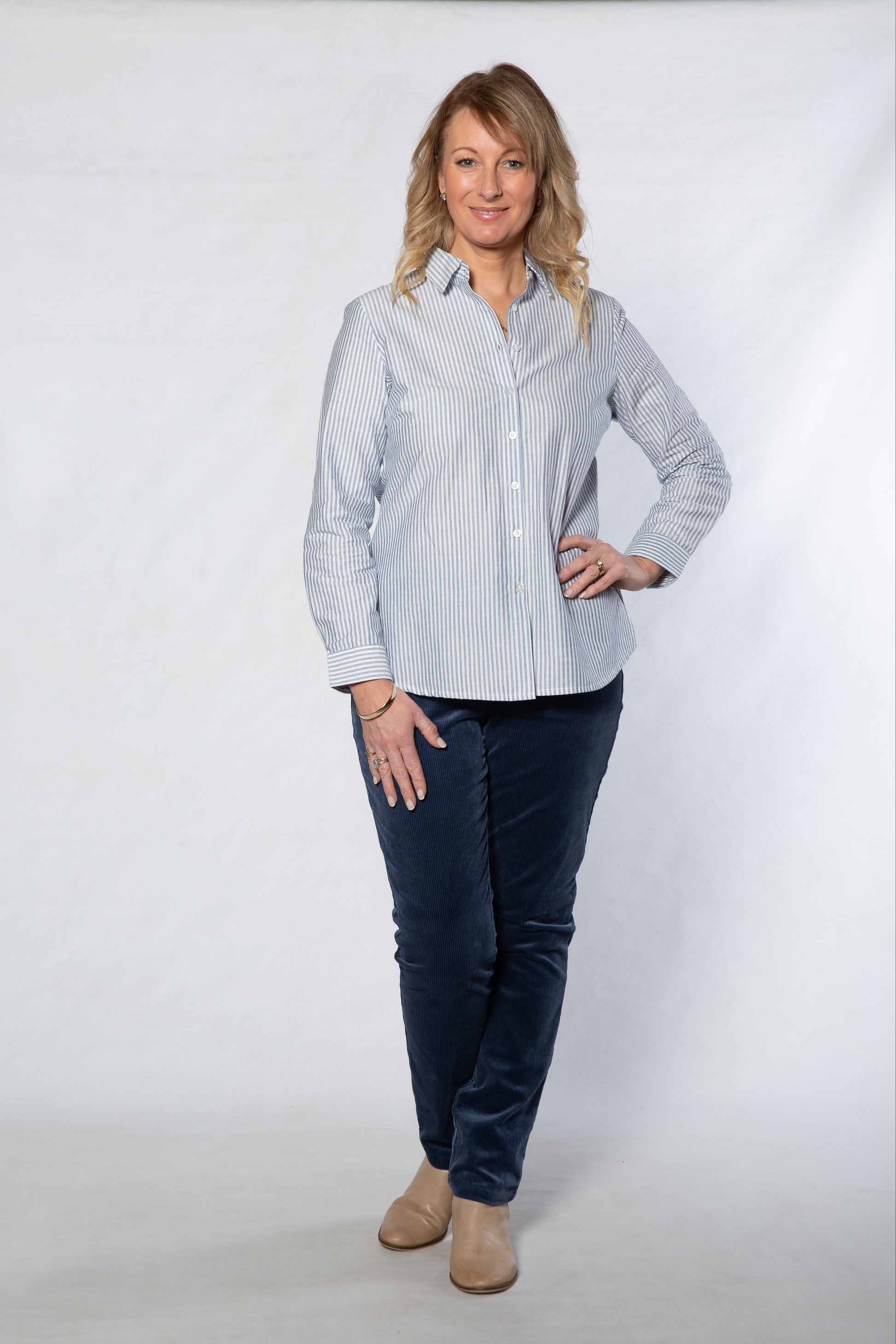 Woman wearing a light blue striped shirt and dark blue pants on a white background