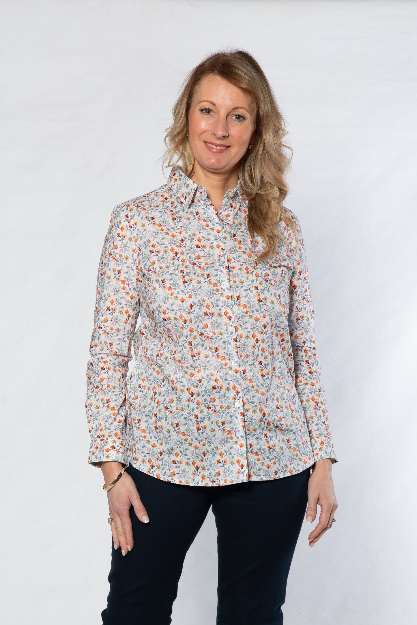 Woman wearing a floral blouse and dark jeans against a white background