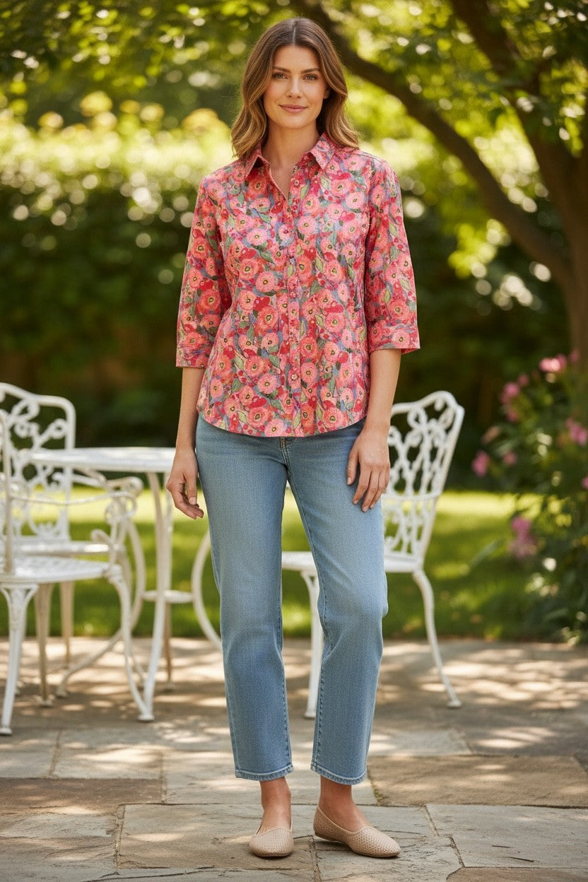 Woman wearing a floral shirt and jeans standing outdoors in a garden setting.