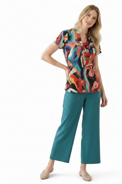 A woman modeling a short-sleeve collared top with a colorful abstract print and teal wide-leg cropped pants against a plain white studio background.