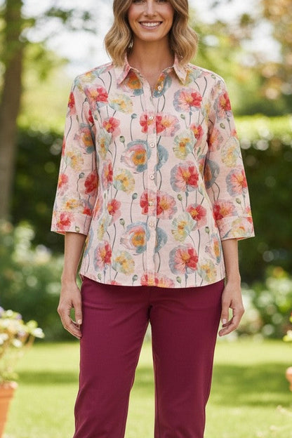 Woman wearing a floral blouse and burgundy pants standing outdoors with plants and greenery in the background
