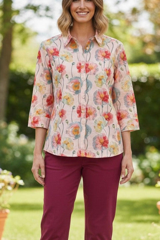 Woman wearing a floral blouse and burgundy pants standing outdoors with plants and greenery in the background