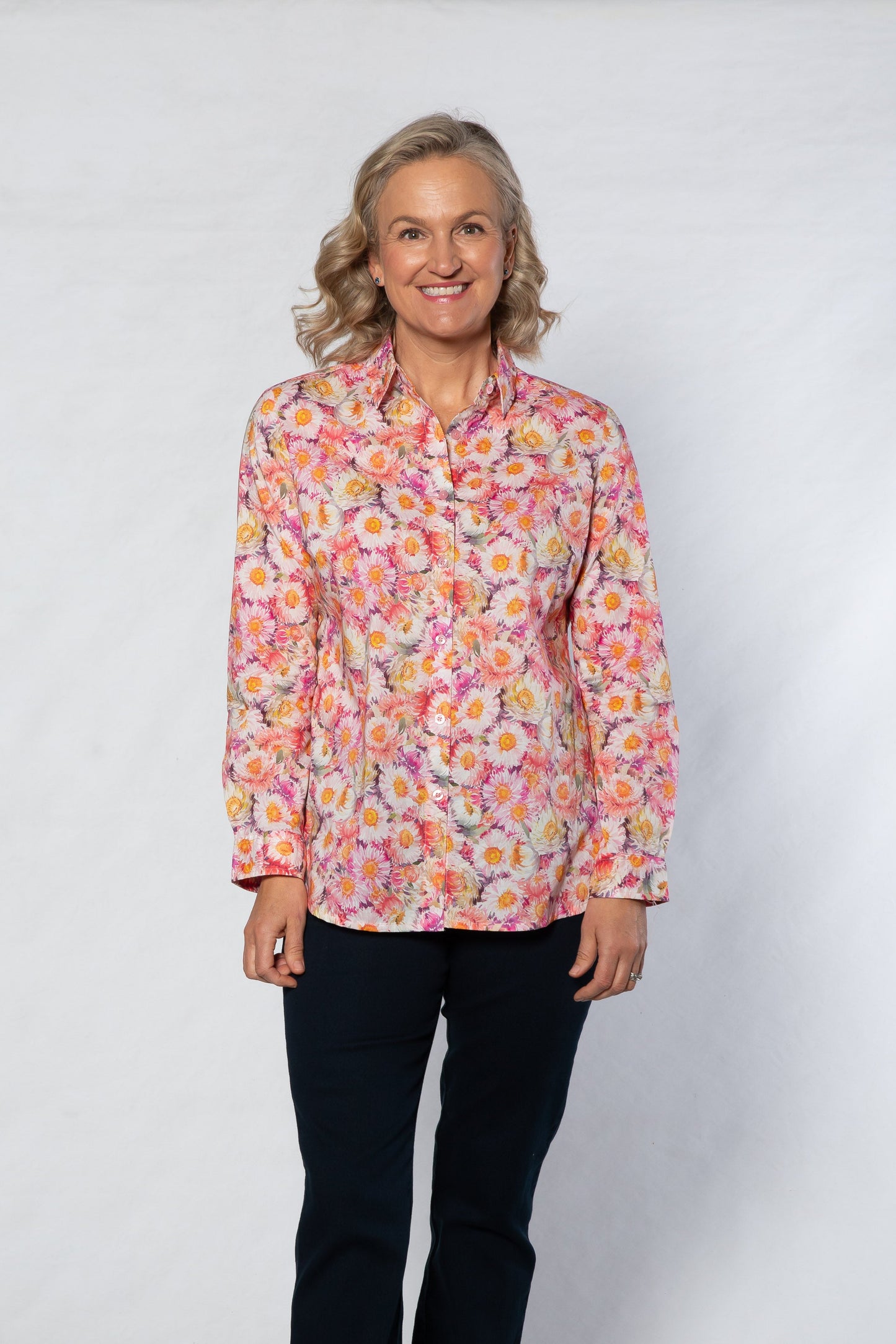 Woman wearing a floral blouse and black pants against a white background