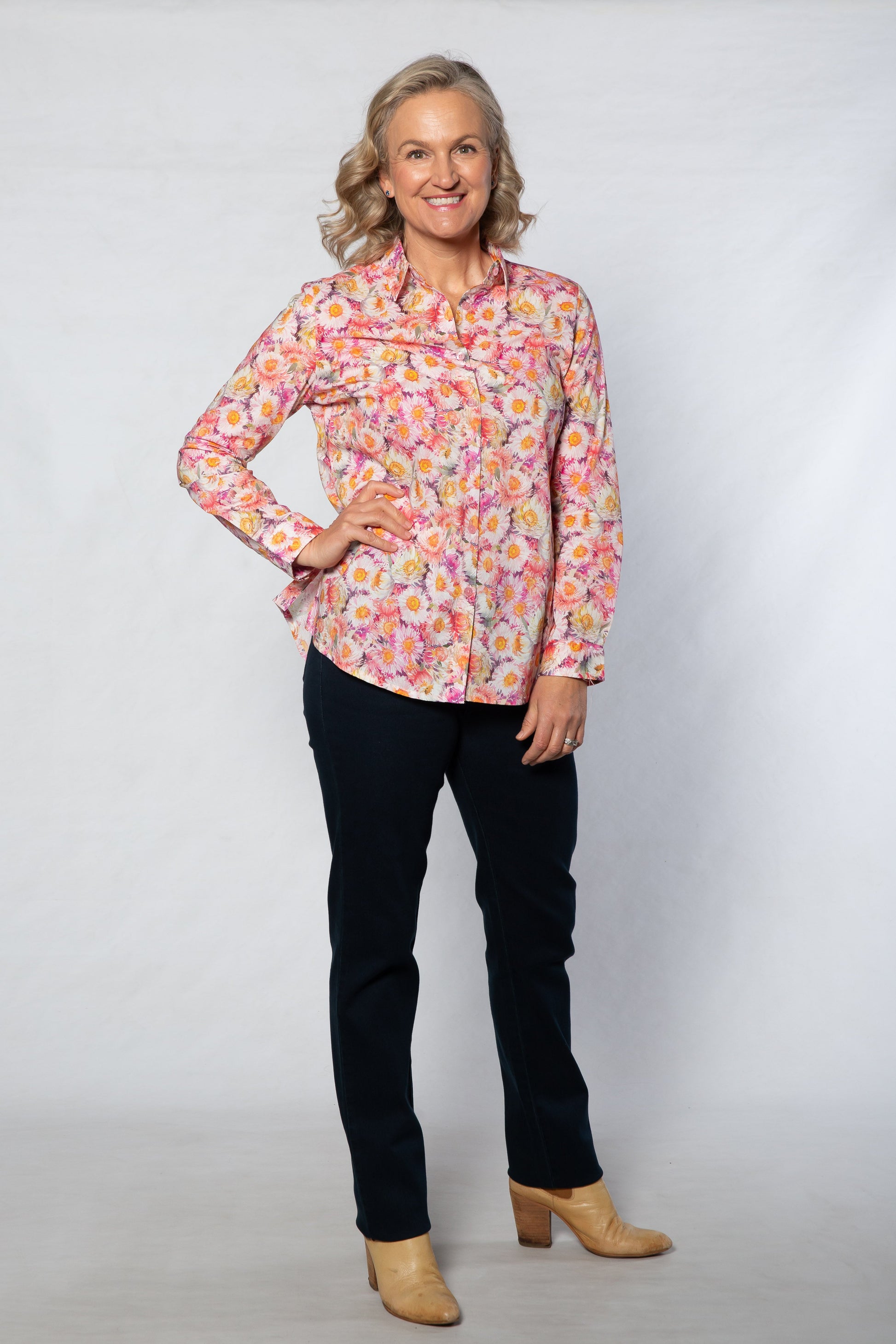 Woman wearing a colorful floral blouse and black pants against a white background