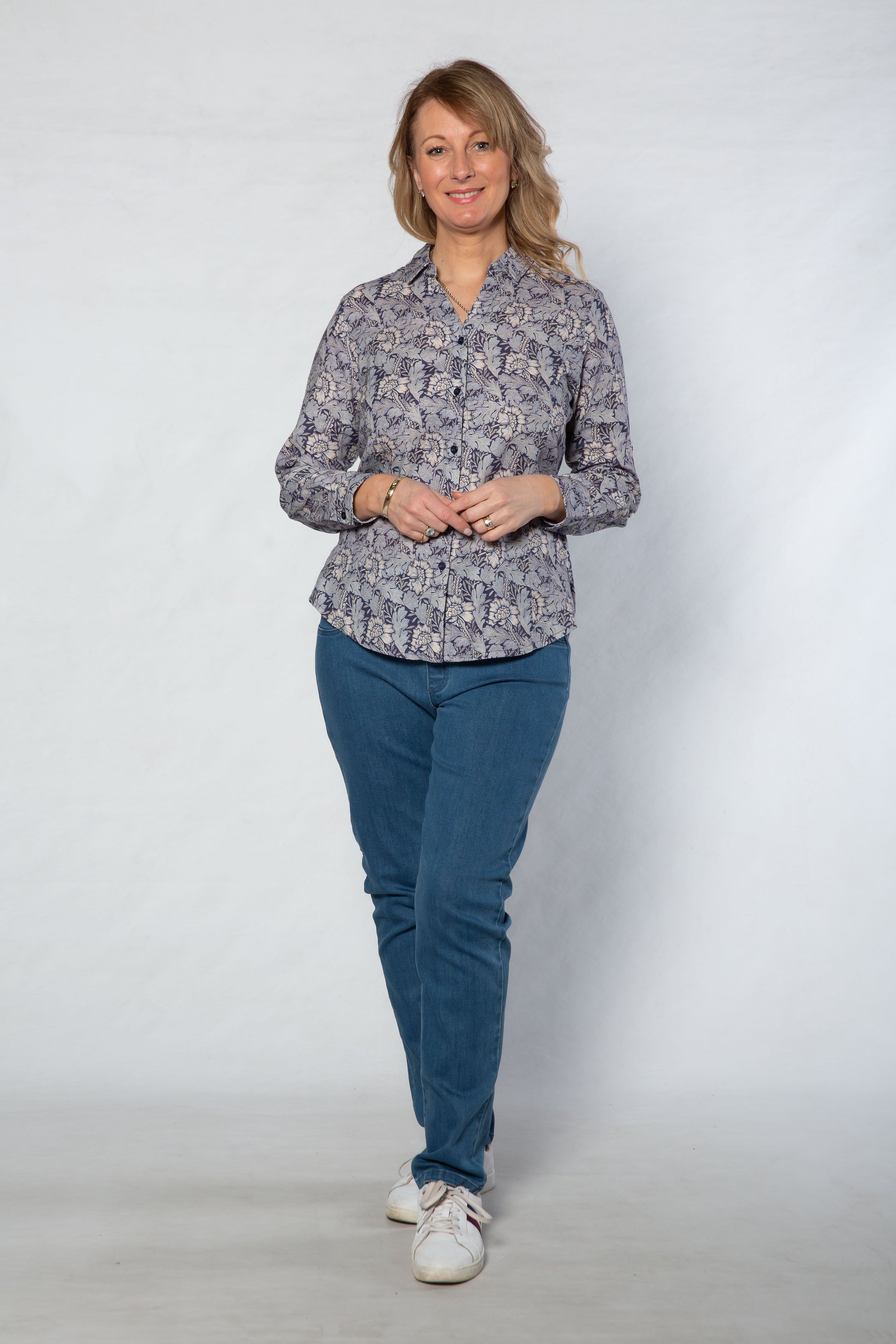 Woman wearing a patterned shirt and blue pants on a white background