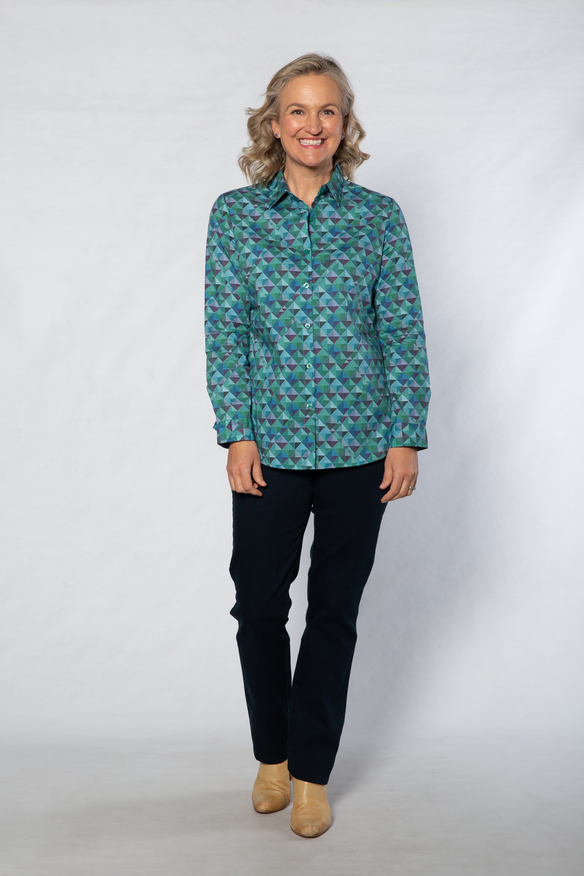 Person wearing a patterned teal shirt and black pants on a white background