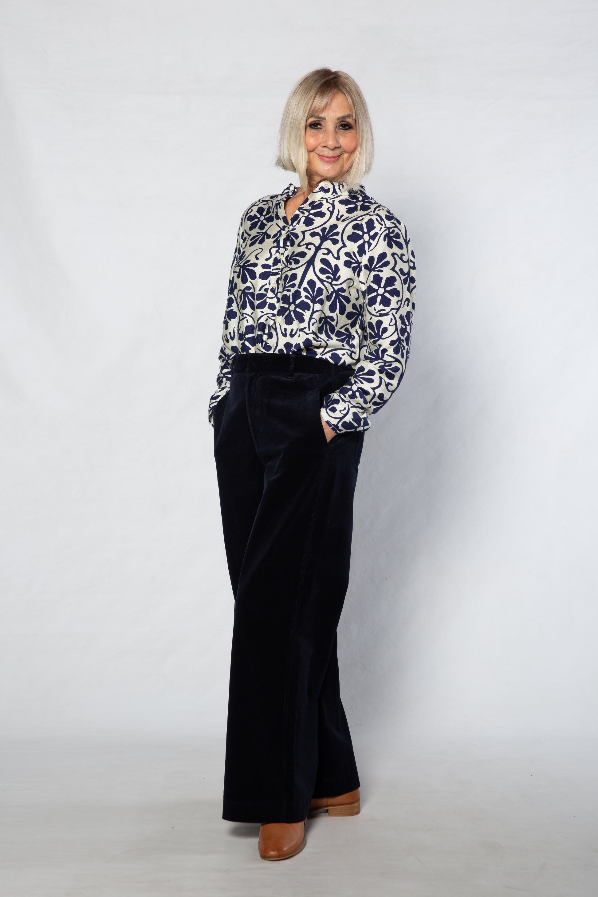 Woman wearing a patterned blouse and black pants against a white background