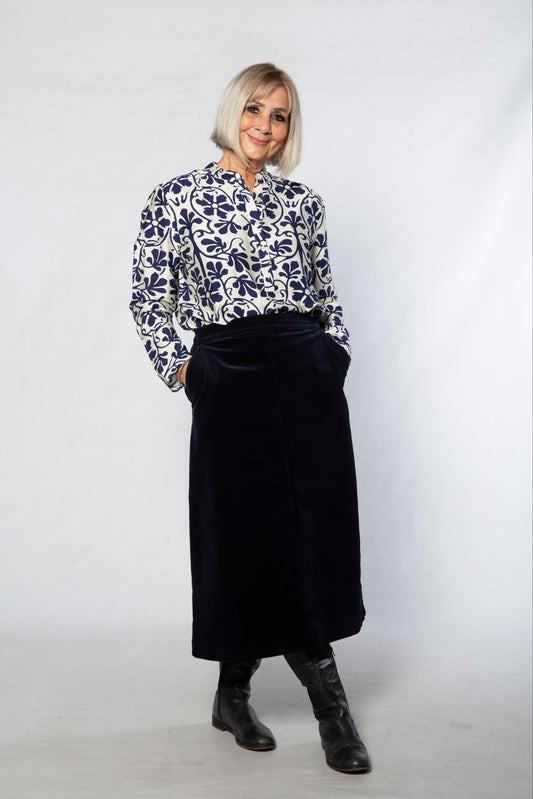 Person wearing a patterned blouse and black skirt against a white background