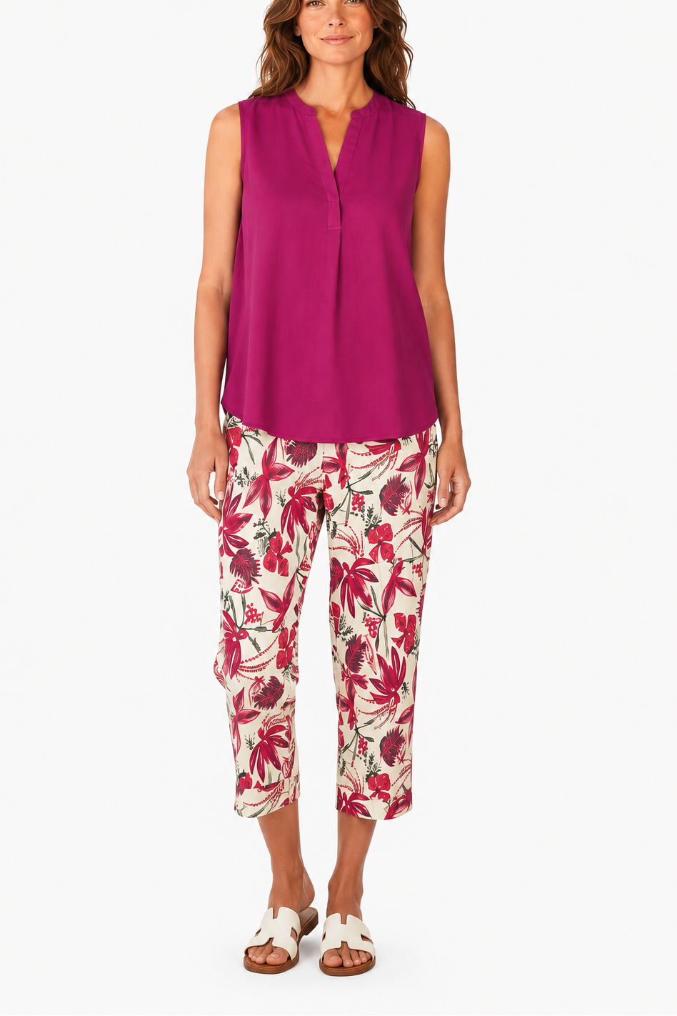 Woman wearing a bright pink sleeveless top and floral pants on a white background