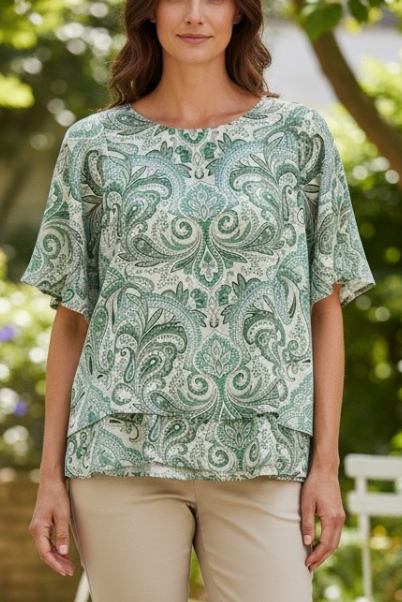 Woman wearing a green paisley patterned top with beige pants outdoors.