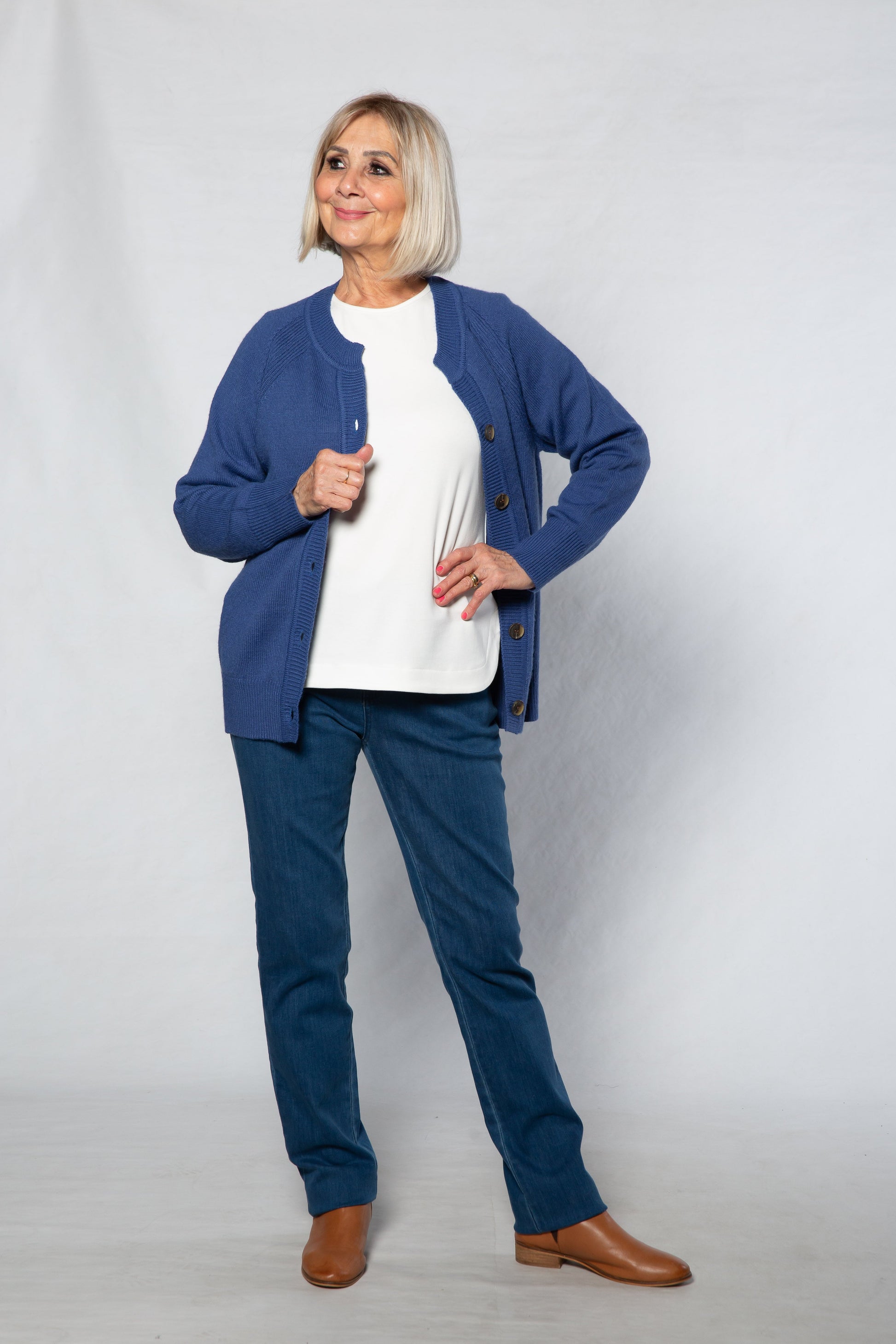Woman wearing a blue cardigan, white shirt, and blue pants on a white background