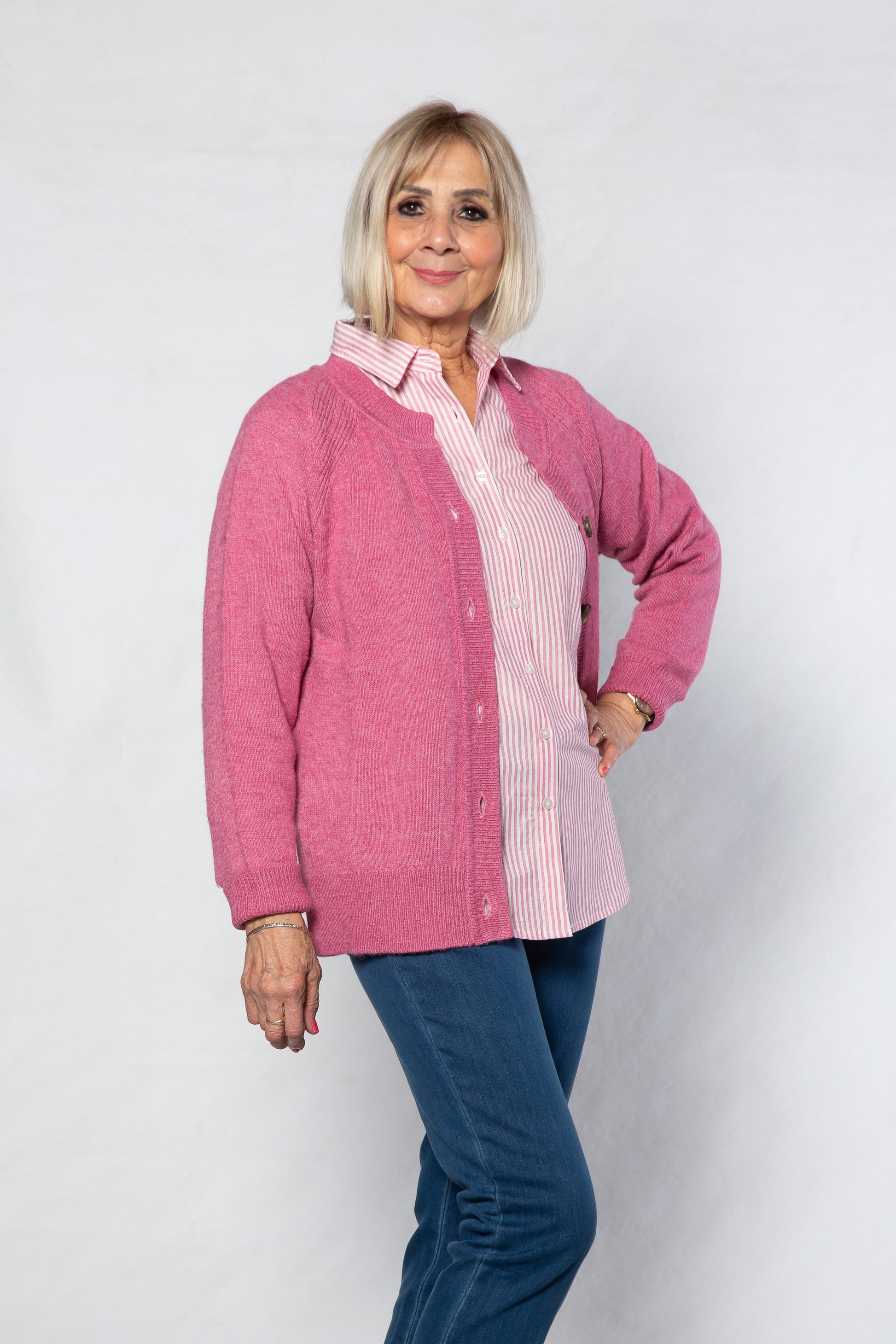 Woman wearing a pink jacket over a checkered shirt with blue jeans on a white background