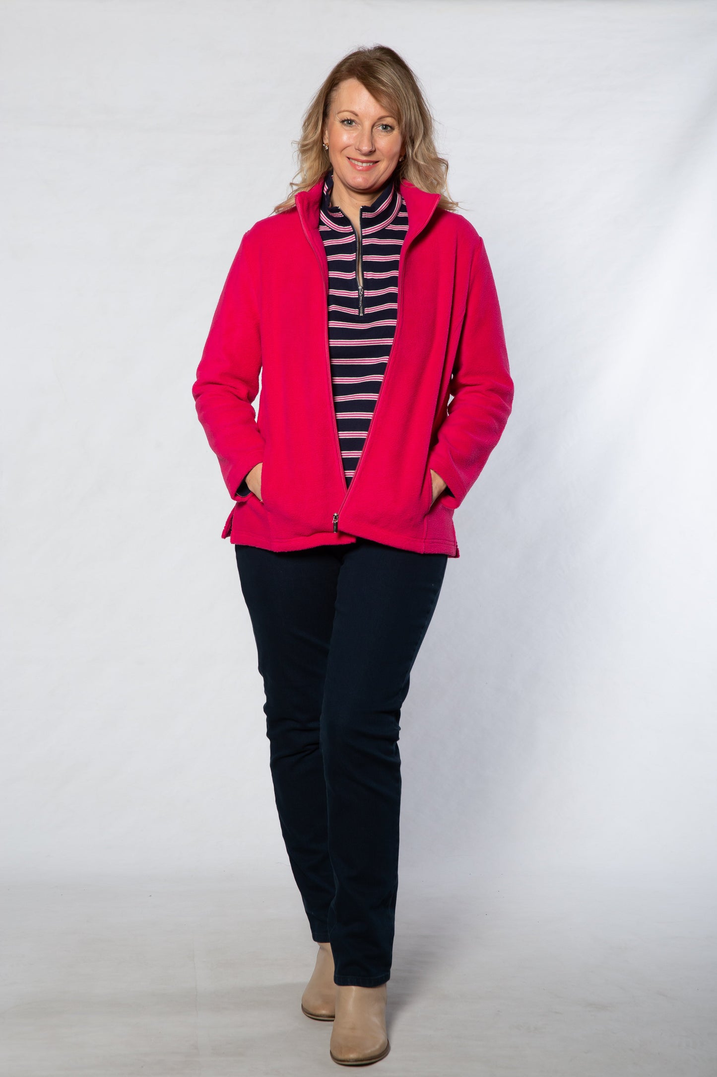 Woman wearing a bright pink jacket over a striped shirt on a white background