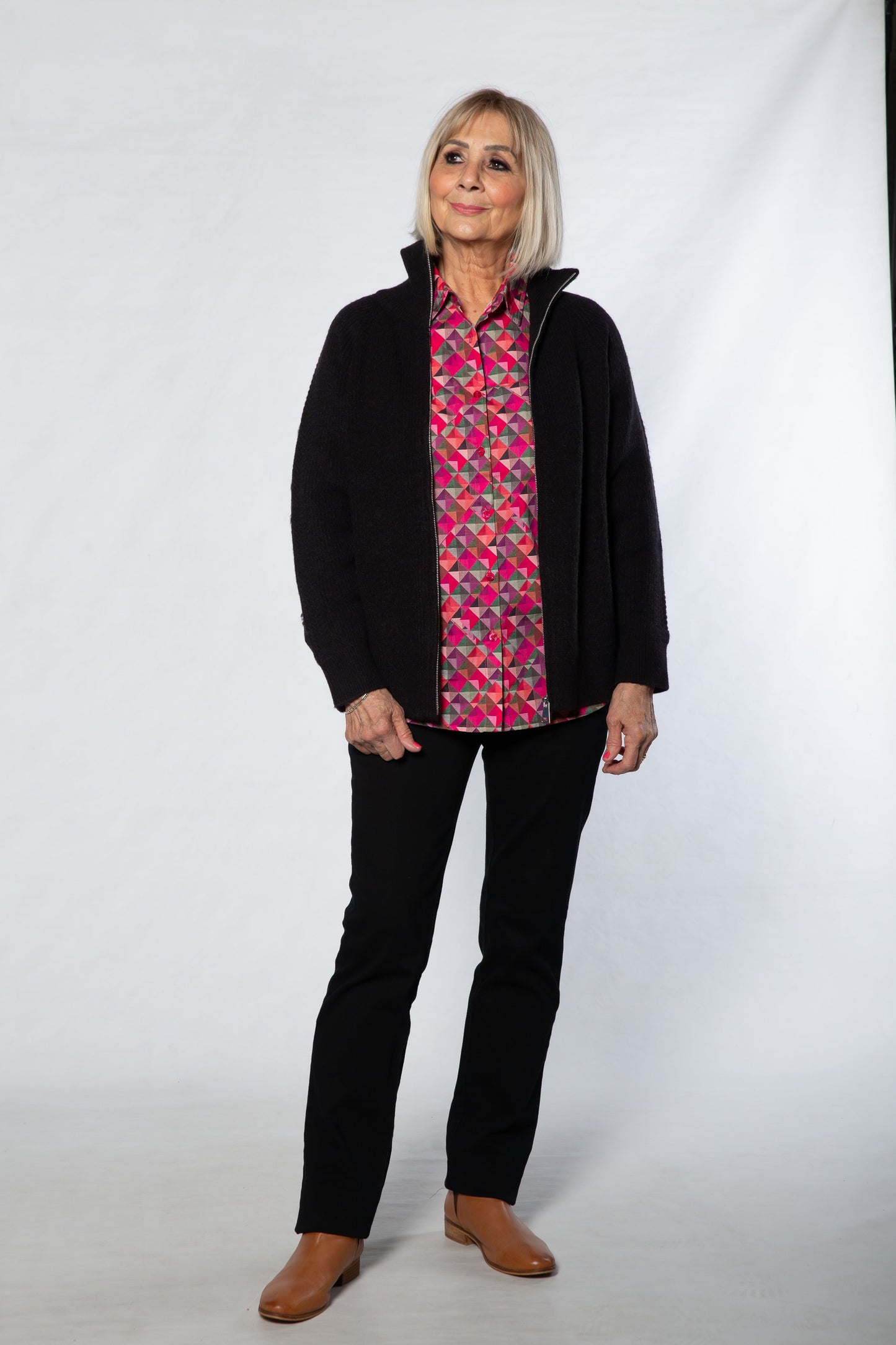 Person wearing a black jacket and patterned shirt on a white background