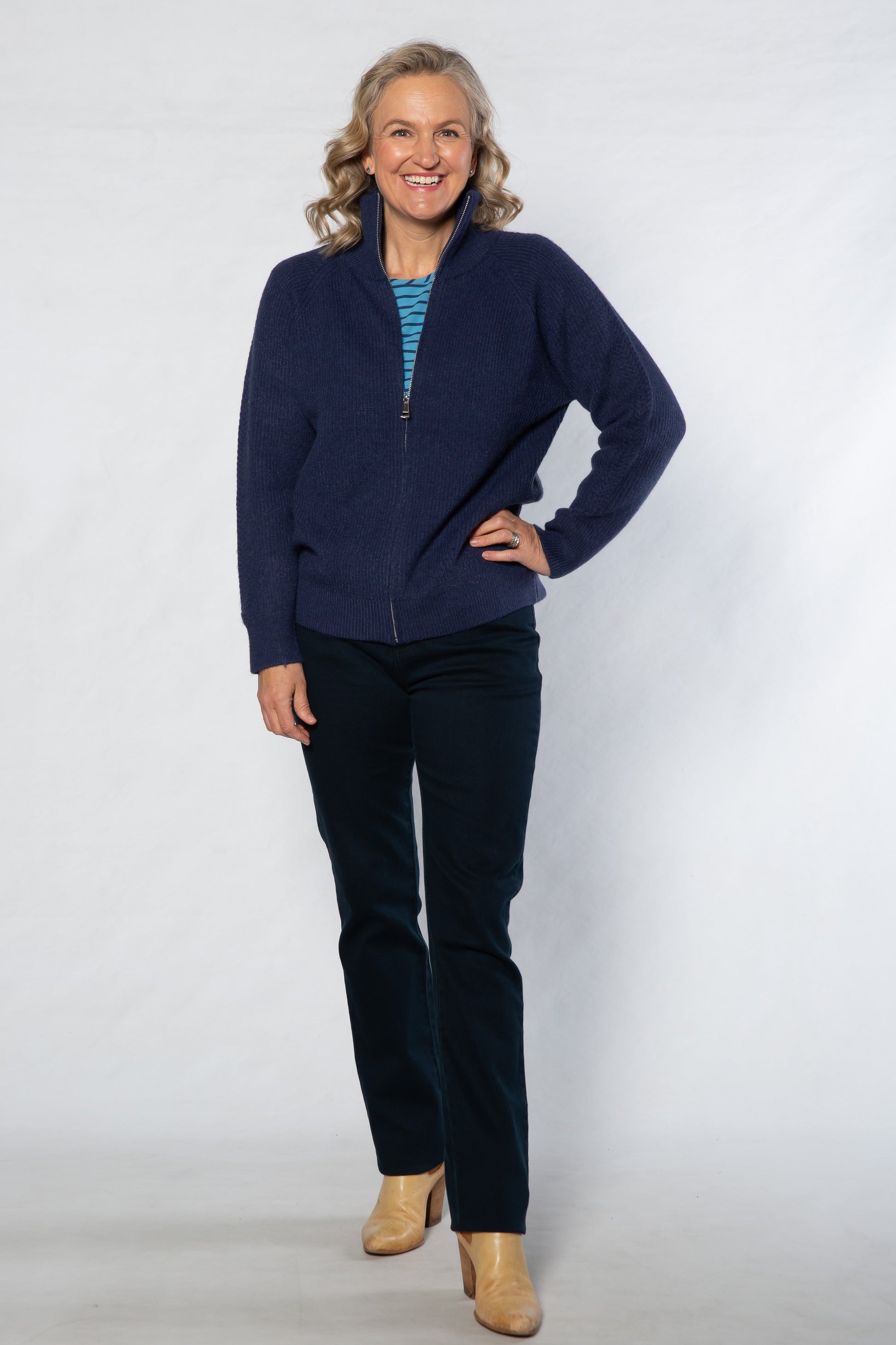 Woman wearing a navy blue sweater and pants with beige shoes on a white background