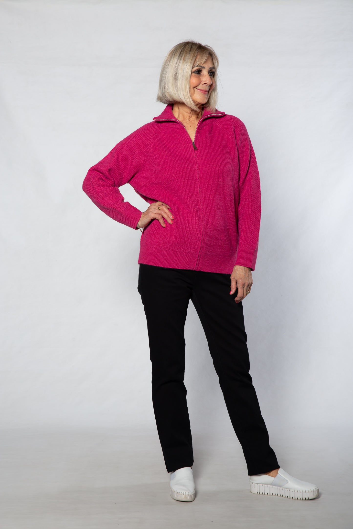 Woman wearing a pink jacket, black pants, and white shoes on a white background
