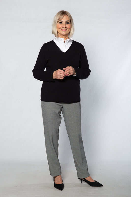 Woman wearing a black sweater, white shirt, gray pants, and black shoes on a white background