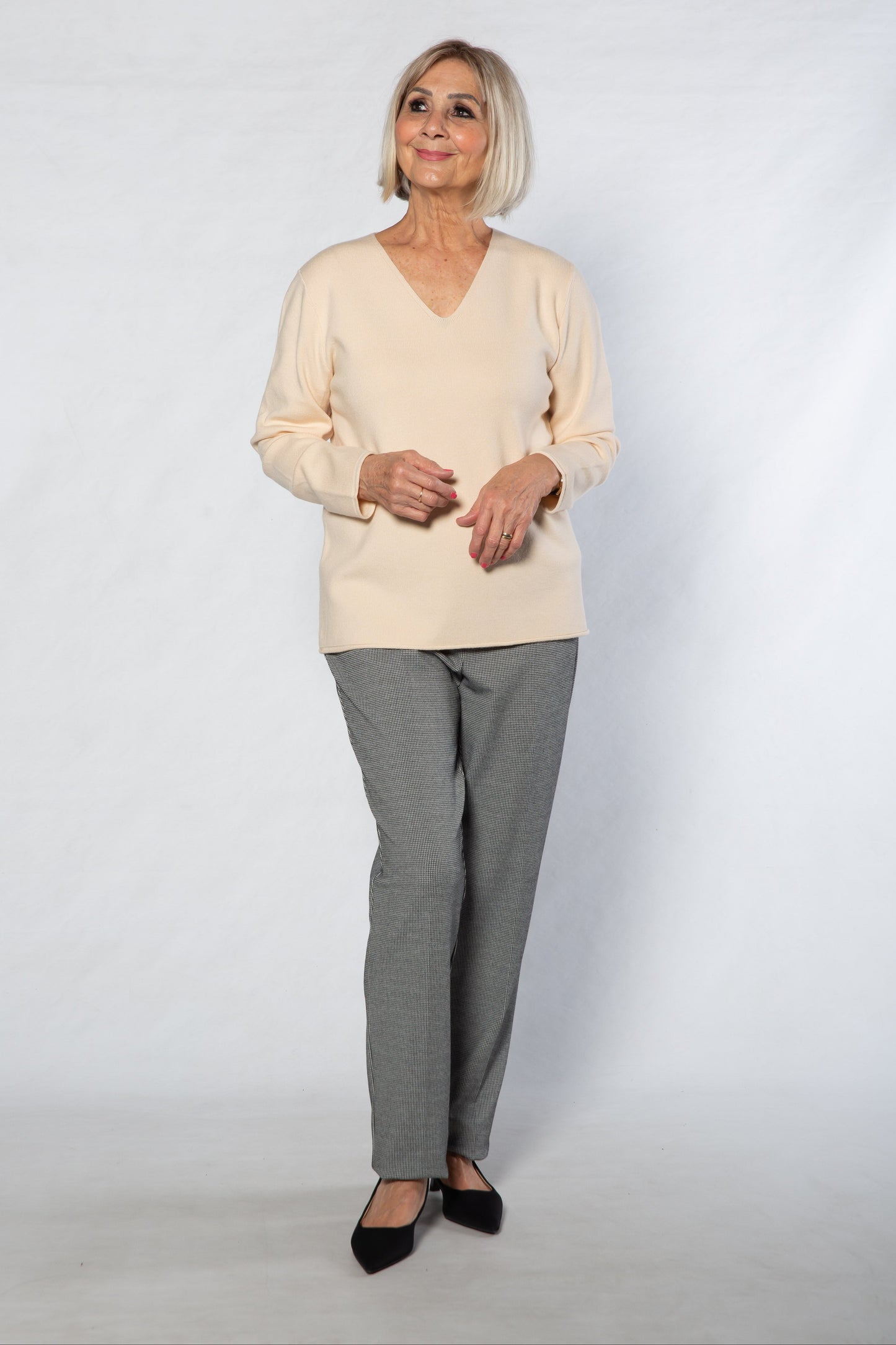 Woman wearing a beige sweater and gray checkered pants on a white background