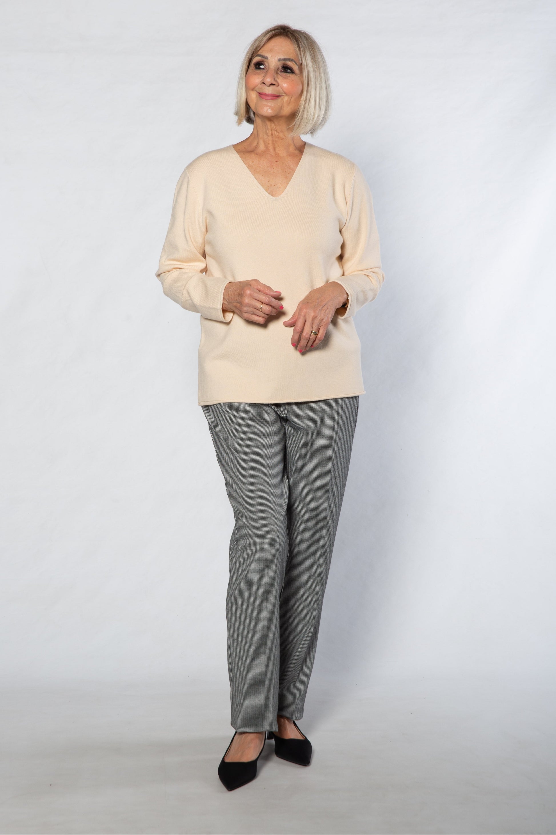 Woman wearing a beige sweater and gray checkered pants on a white background