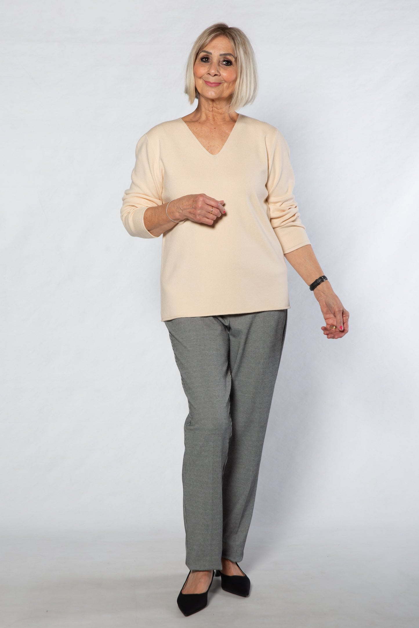 Woman wearing a beige sweater and gray checkered pants on a white background