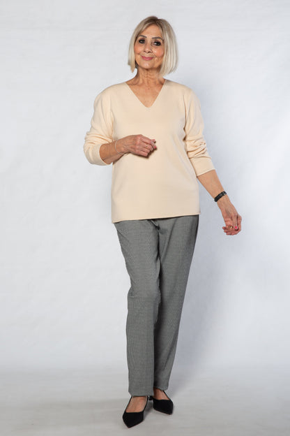Woman wearing a beige sweater and gray checkered pants on a white background