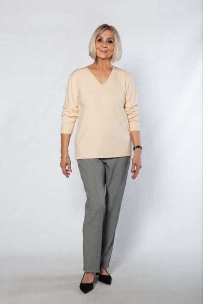 Woman wearing a beige sweater and gray checkered pants on a white background