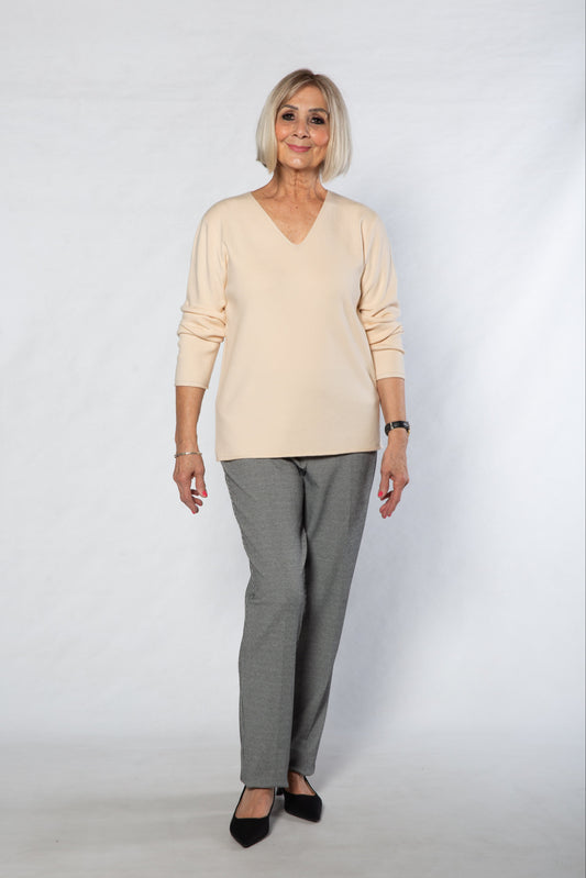 Woman wearing a beige sweater and gray checkered pants on a white background