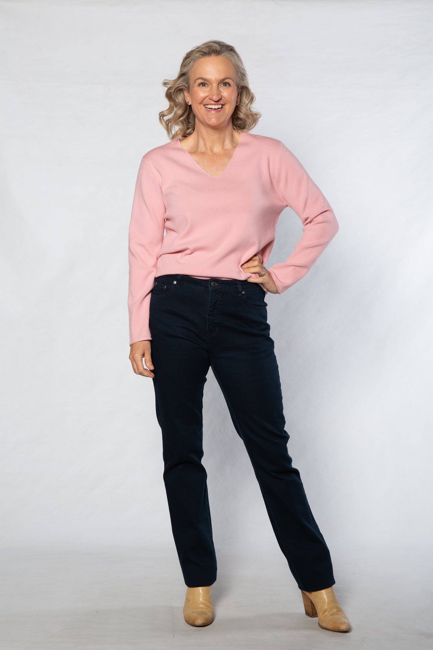 Woman wearing a pink sweater and black jeans on a white background